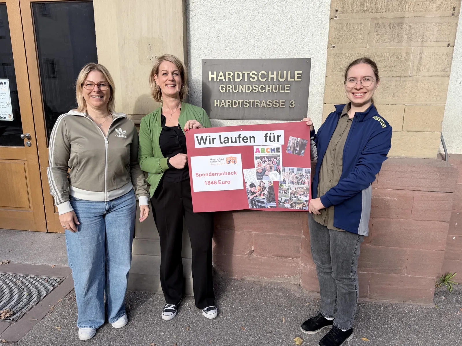 Drei Personen präsentieren vor der Hardtschule einen Spendenscheck über 1.846 Euro für Arche Karlsruhe